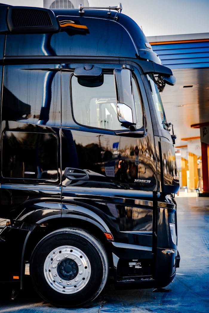 heros-img Sleek black truck parked outdoors at a service station during daytime.