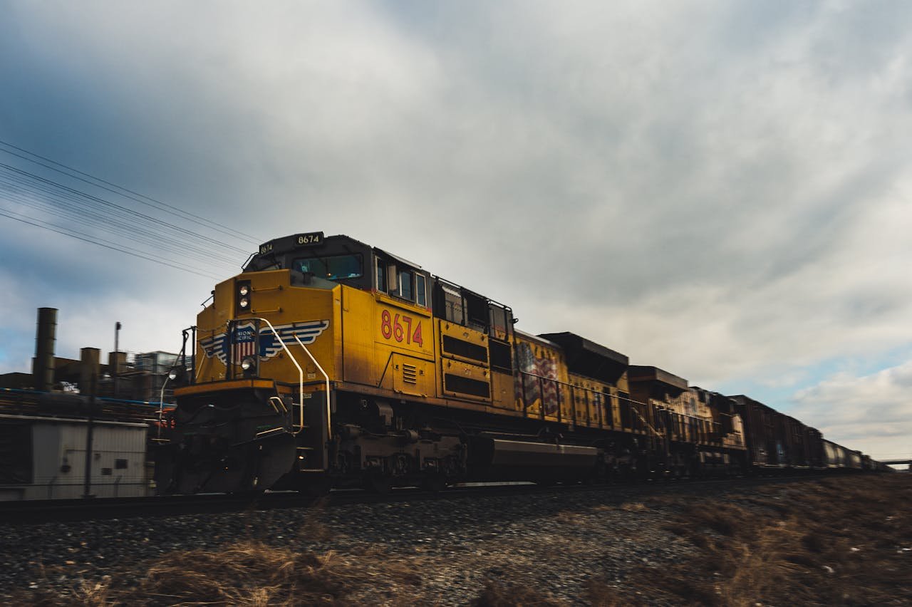 about-us Yellow freight train moving on outdoor railway track under cloudy sky.